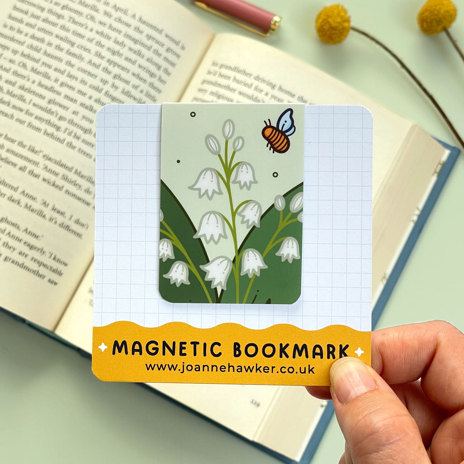 Magnetic bookmark with floral lily of the valley design held over an open book.