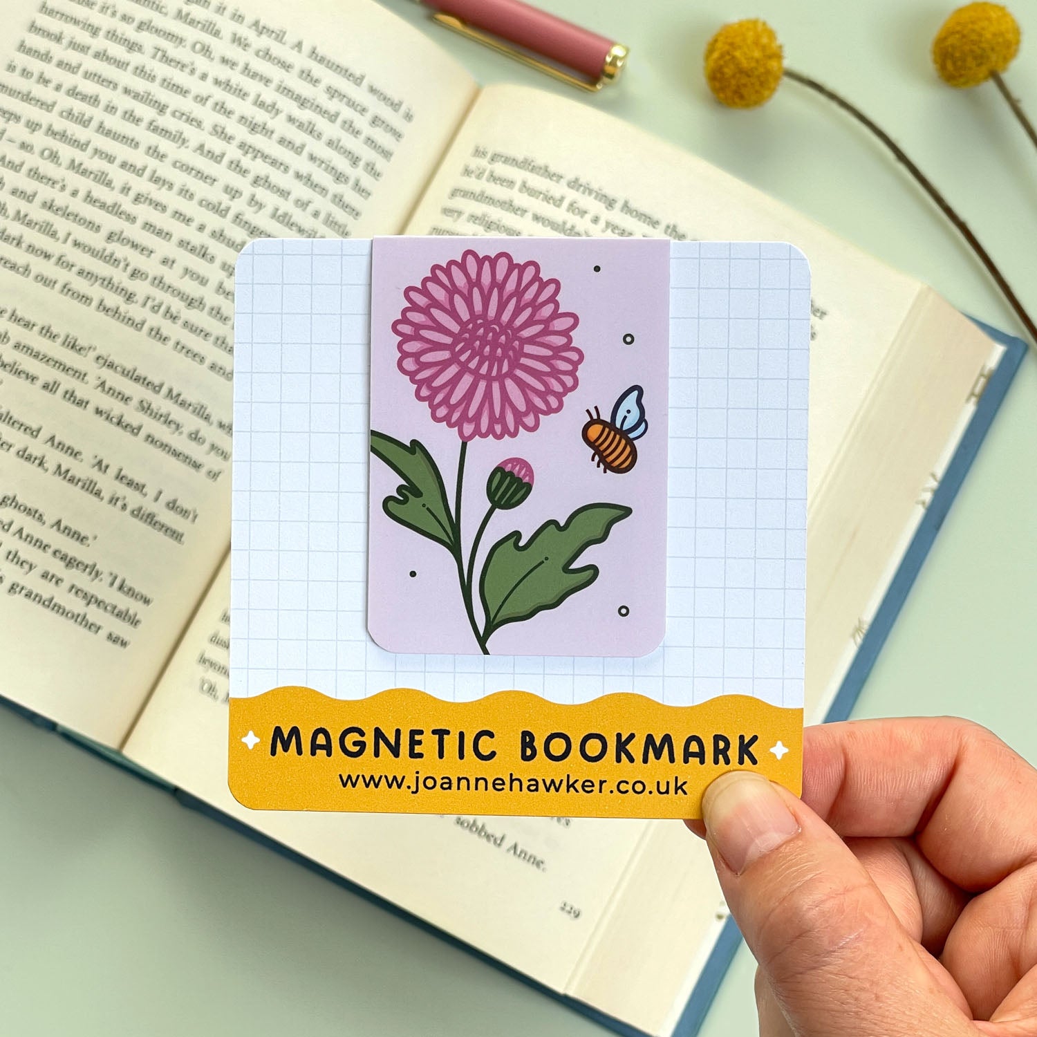 Magnetic bookmark with floral chrysanthemum design held over an open book