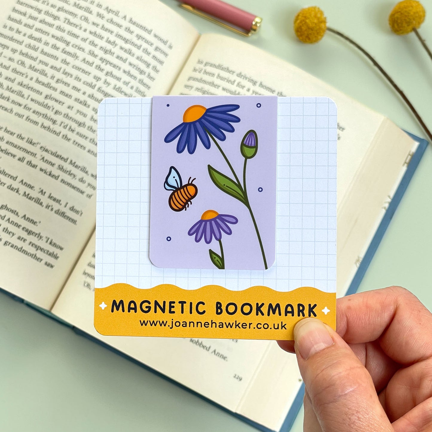 Magnetic bookmark with floral aster design held over an open book