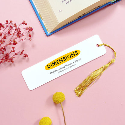 A blank metal bookmark giving the rough dimensions of each bookmark. It has been shot on a pink background with a book and dried flowers.