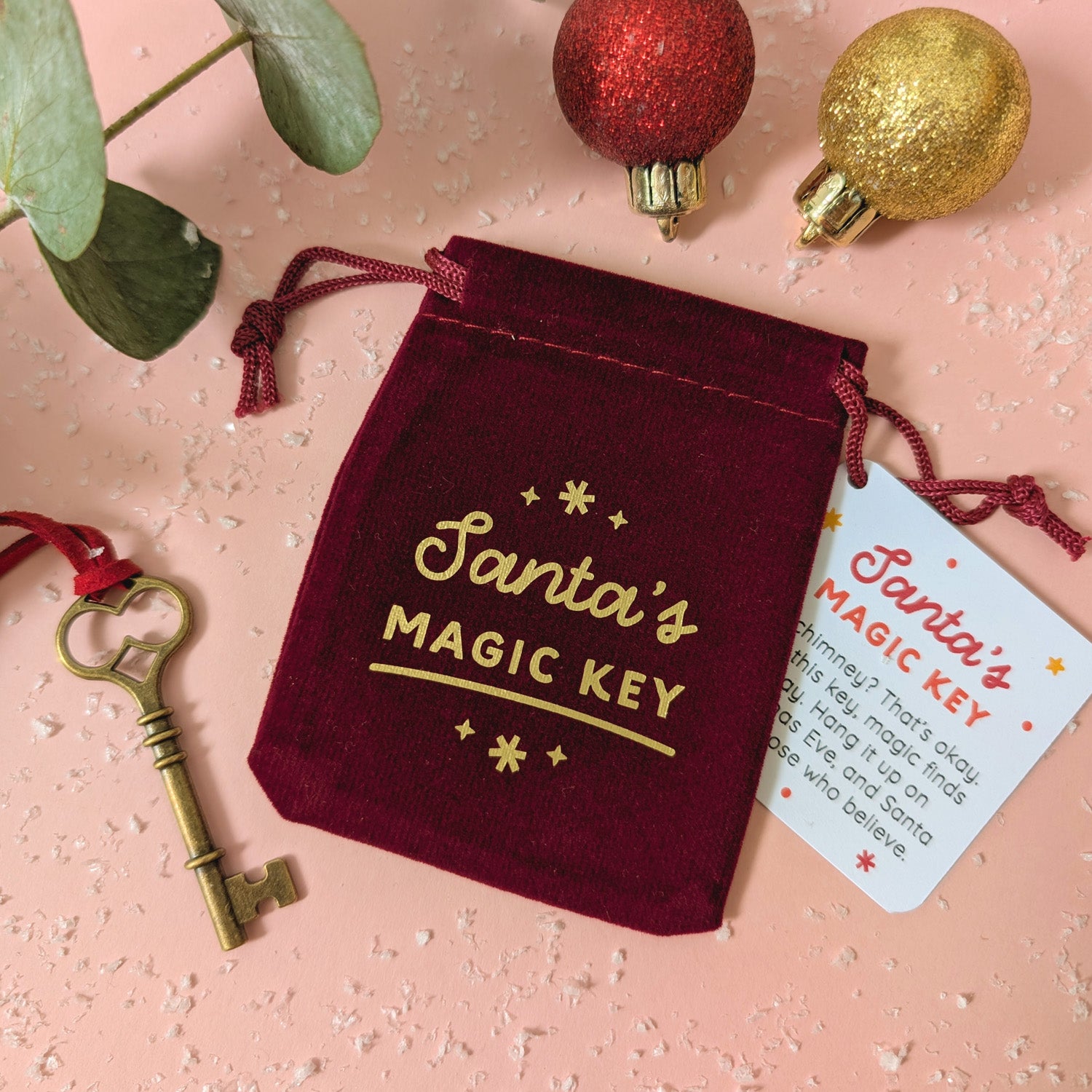 Red velvet pouch with 'Santa's Magic Key' text, key, and tag on a pink background