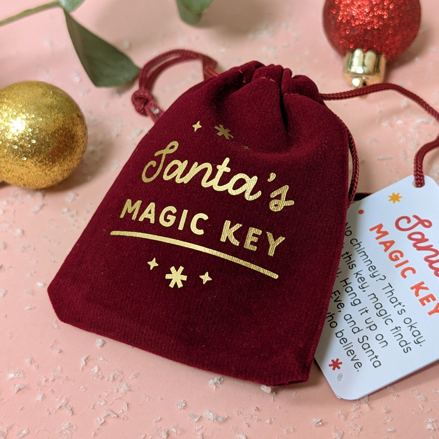 Red drawstring bag with 'Santa's Magic Key' text on a pink background with Christmas decorations.