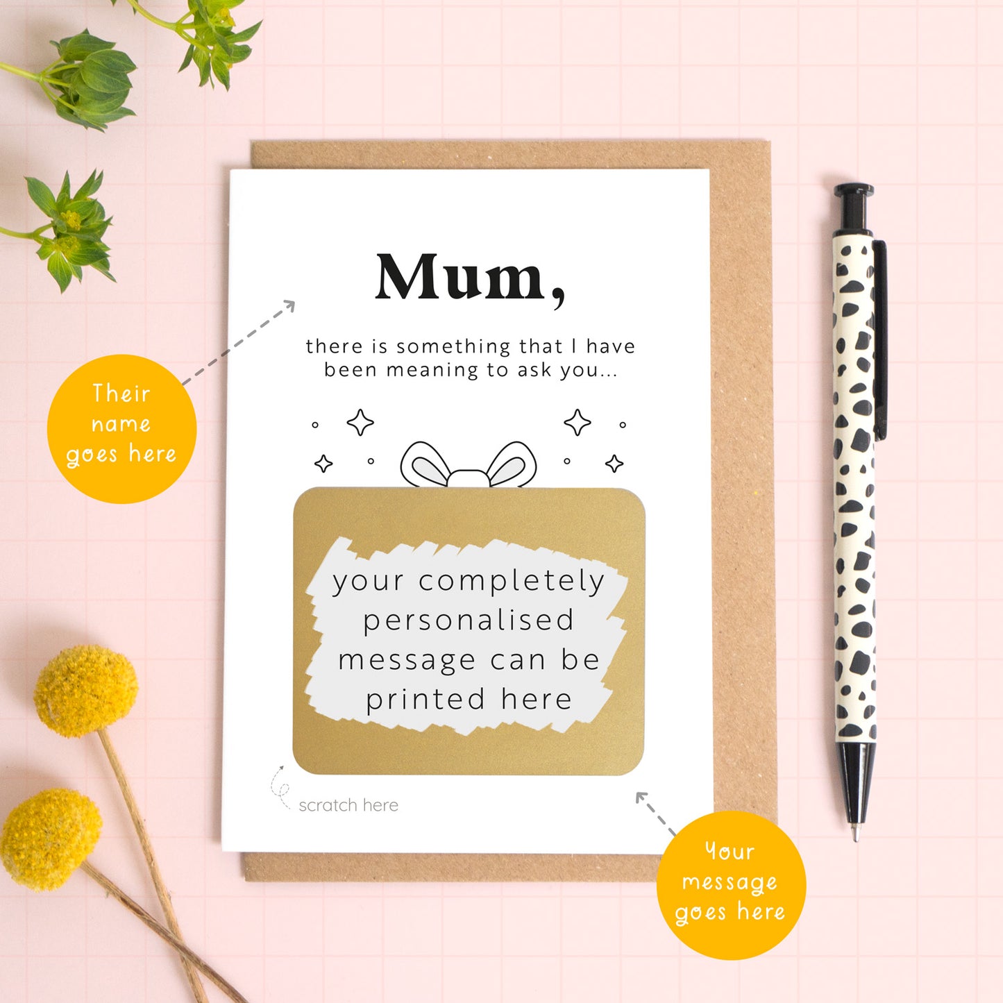 A ‘will you be my birthing partner’ scratch and reveal card photographed lying on a Kraft brown envelope, set upon a pink background surrounded by foliage and a pen for scale. The gold panel has been scratched off to reveal the personalised question and there are orange circles pointing to the areas that can be personalised. These include the name and the scratch off message. 