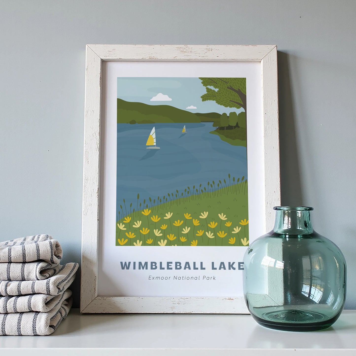 Wimbleball Lake, Exmoor National Park art print in a white frame on a light grey background with a pile of cloths and blue vase.