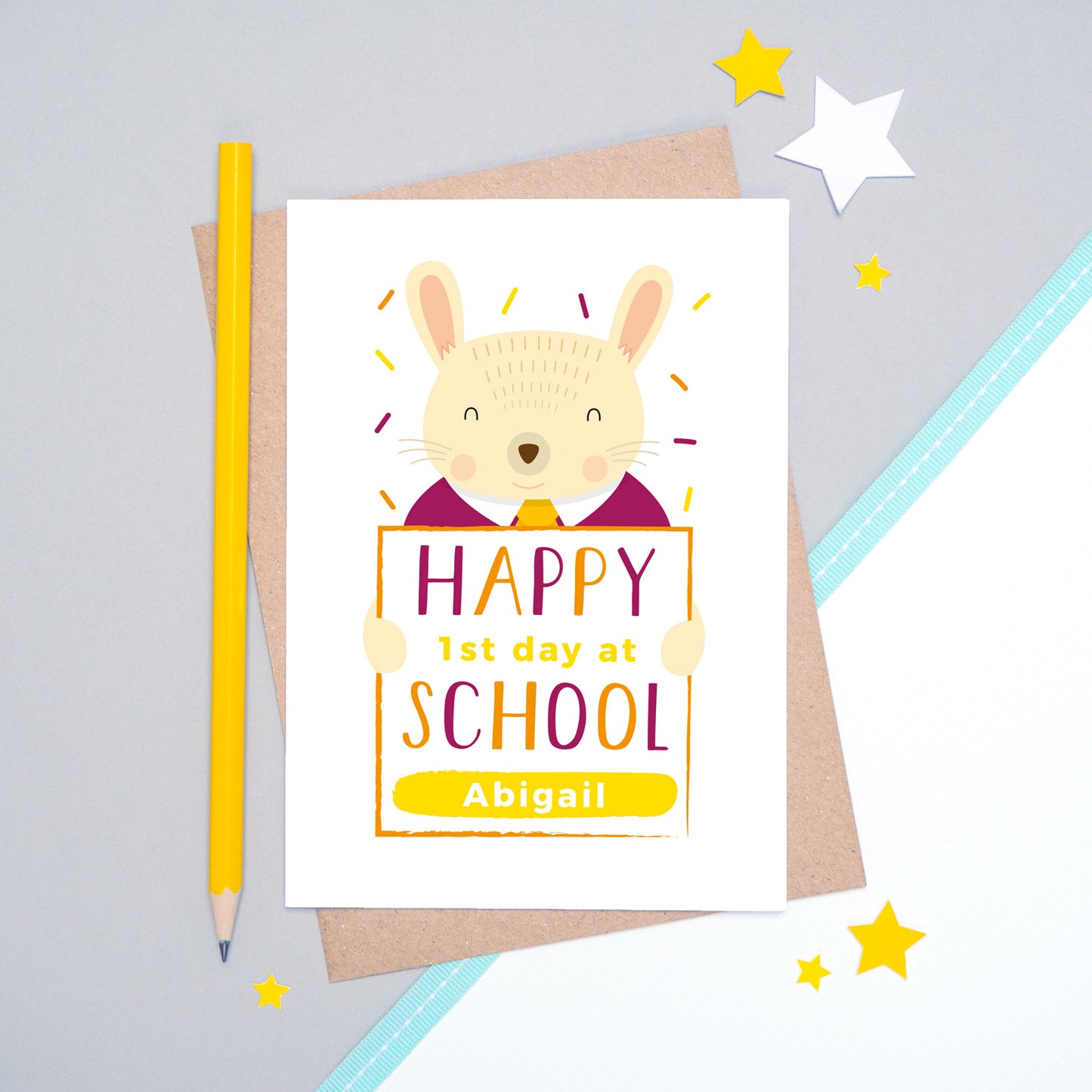 A happy 1st day at school personalised card featuring a friendly rabbit sat on a grey and white background.