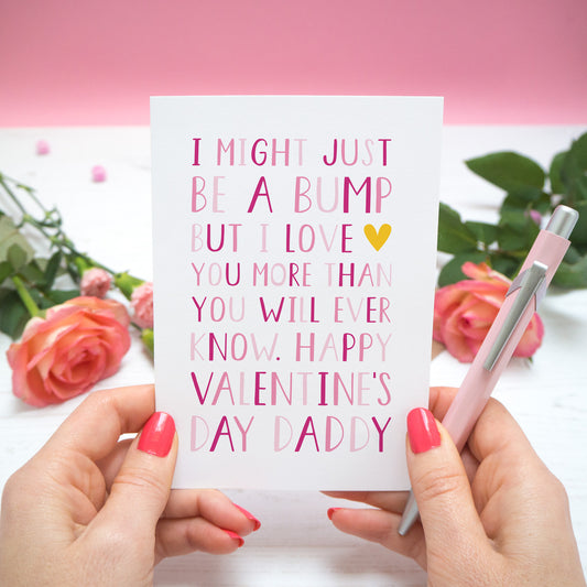 A valentine's card from the 'bump' with text in different shades of pink that reads "I might just be a bump but I love you more thank you will ever know. Happy Valentine's day Daddy." The card is held in two hands and there are roses in the background.