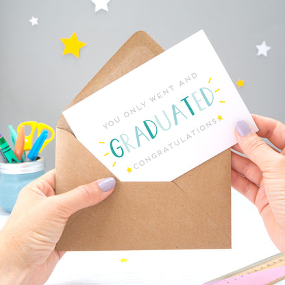 You only went and graduated congratulations card being pulled from an envelope by Joanne Hawker in front of a grey background with white and yellow stars. The typography is a mix of grey and varying tones of blue.