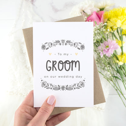 To my groom on our wedding day. A white card with grey hand drawn lettering, and a grey floral border. The image features a wedding dress and bouquet of flowers.