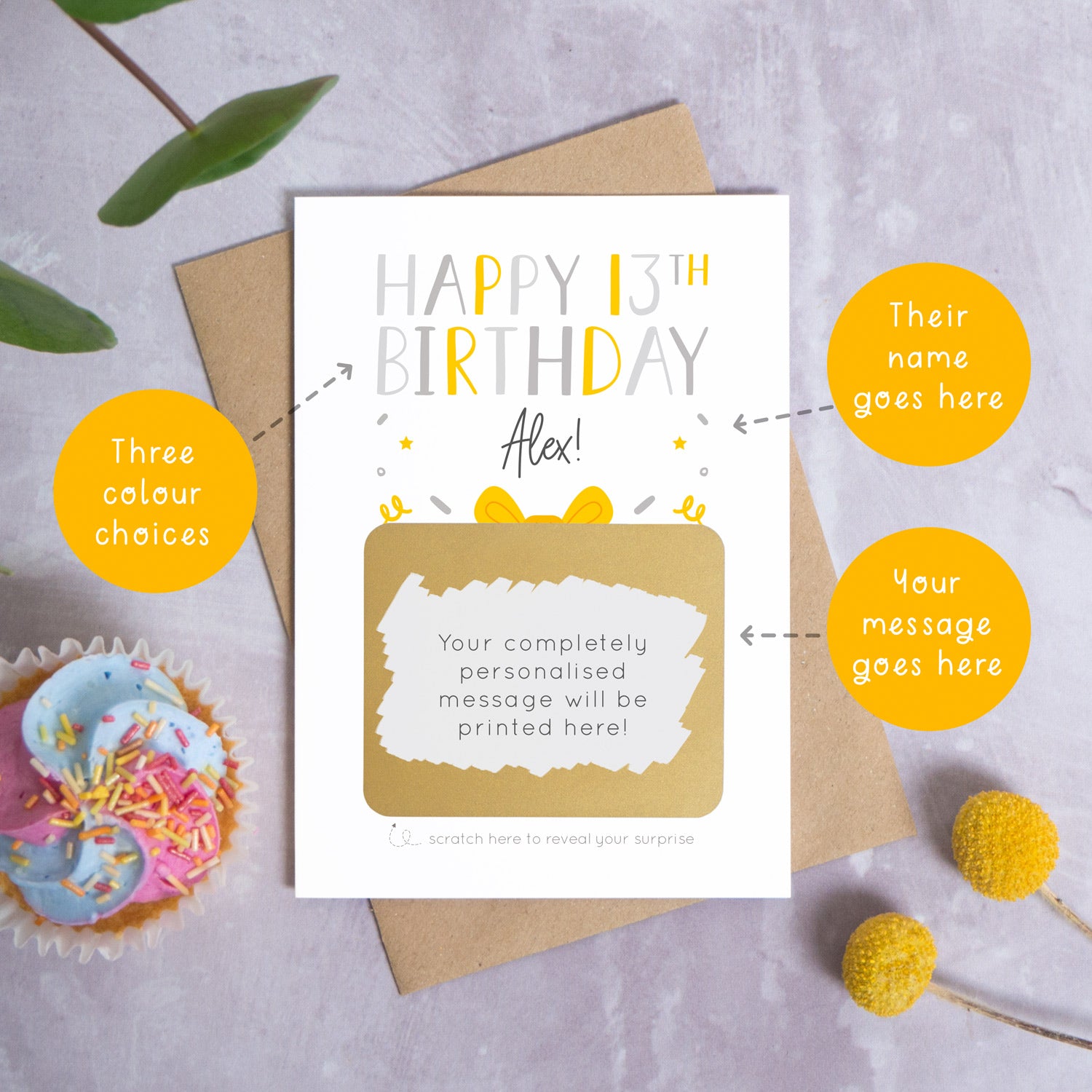 A personalised happy 13th birthday scratch card in grey that has been photographed on a grey background with foliage and a cupcake. There are also orange circles laid over the top of this image with arrows pointing to the areas that can be customised. In this instance they point to the name, the colour choices and the personalised scratch off message.