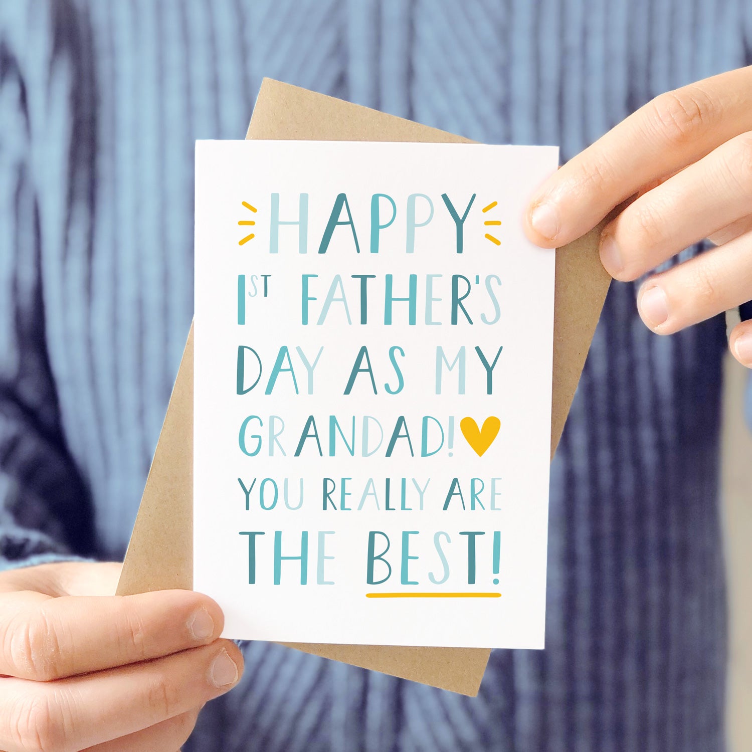'Happy 1st Father's Day as my Grandad! You really are the best!' Photographed being held in front of a man wearing a grey blue knitted jumper and being held with it's kraft brown envelope.