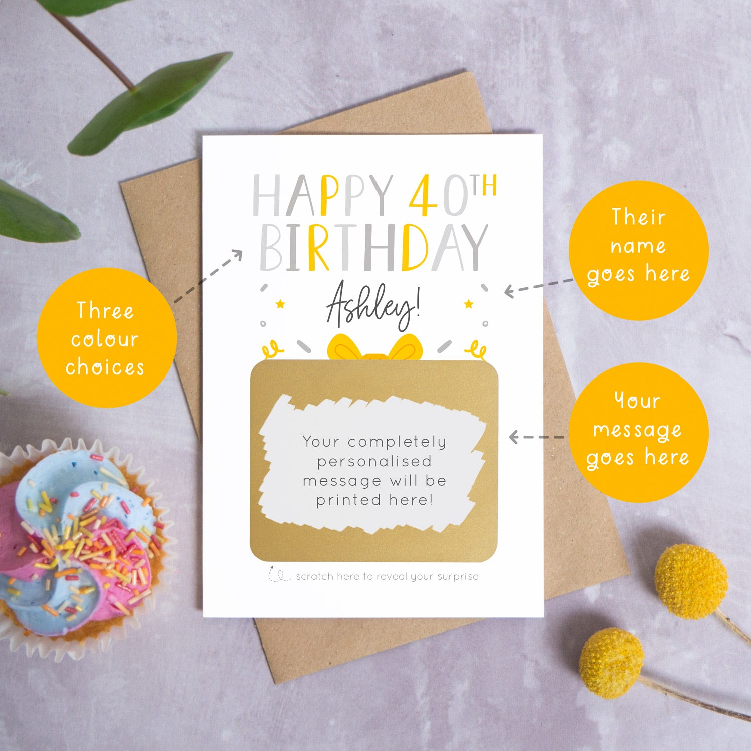 A personalised happy 40th birthday scratch card in grey that has been photographed on a grey background with foliage and a cupcake. There are also orange circles laid over the top of this image with arrows pointing to the areas that can be customised. In this instance they point to the name, the colour choices and the personalised scratch off message.