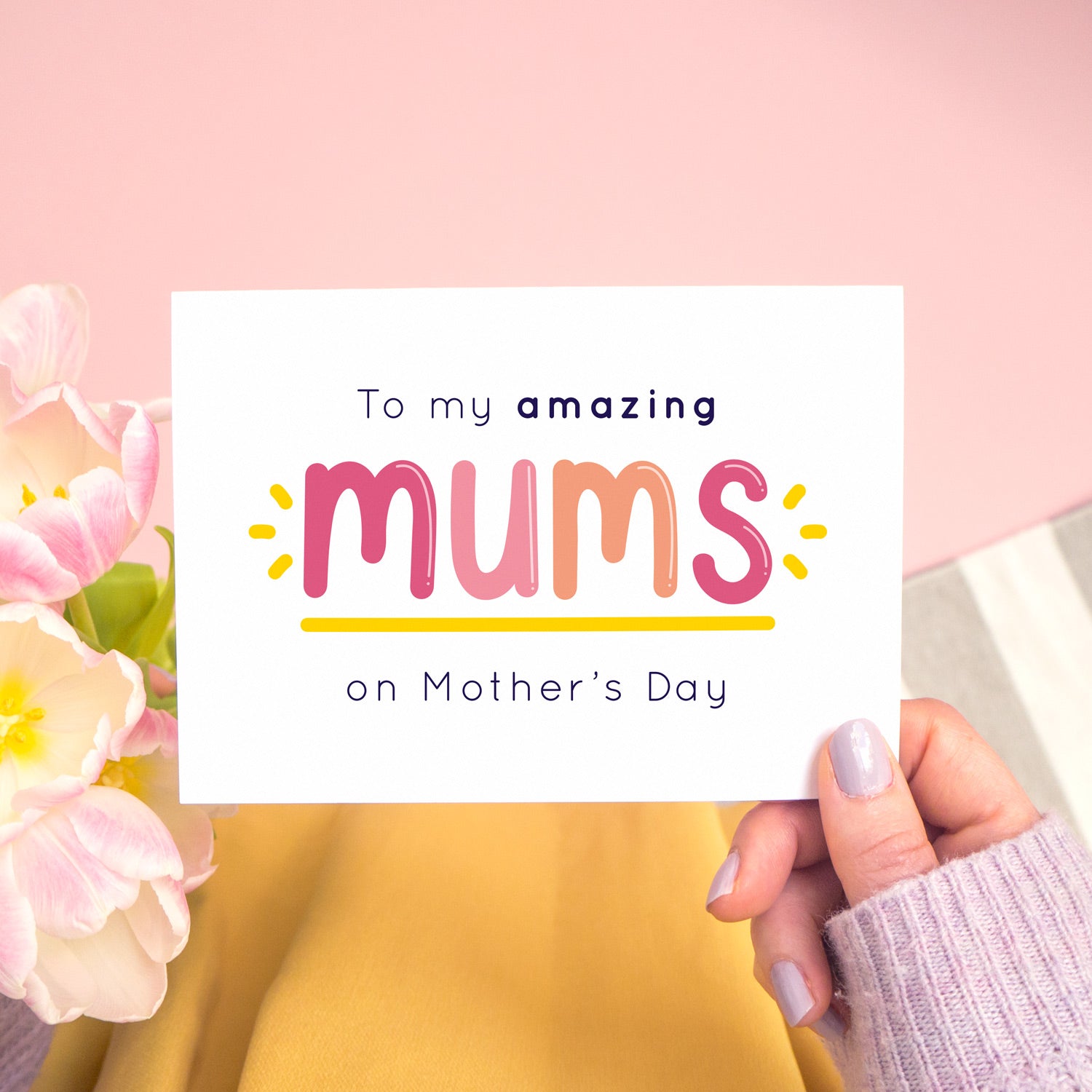 An amazing mums mother’s day card designed for those lucky enough to have two mums! This card is being held over a pink background with tulips to the left and a hand wearing purple nail varnish to the right. This card is in the pink and peach colour palette.
