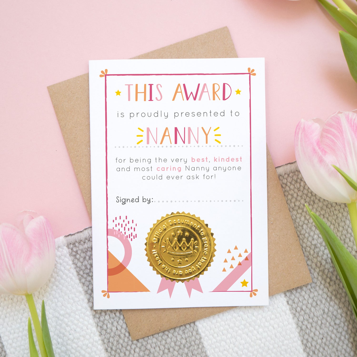 A mother's day certificate for Nanny showing the card before a child has written on the front. This is how your card will arrive. It has been shot over head on a kraft brown envelope with a pink and white and grey background with tulips.