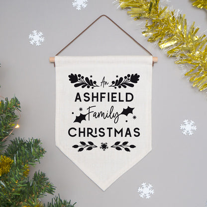 An example of the family Christmas flag with the word 'An' instead of 'A'. The flag is shot on a grey background with festive decor and white snow flakes.