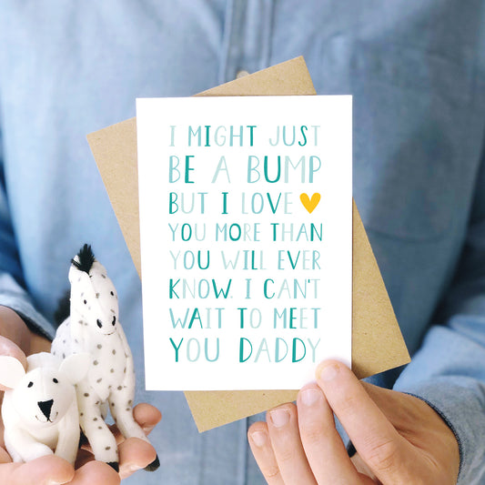 I can't wait to meet you card from the bump to daddy fathers day card photographed being held by a man in a blue button up shirt and with two cuddly toys. This design is shown in varying tones of blue and a pop of yellow.