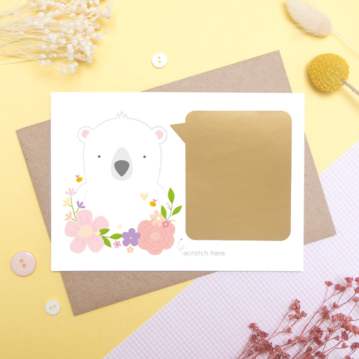 A personalised godparent scratch card before it has been scratched off. This is how the cards will arrive. This one has been shot on a yellow background with floral props. It features a white bear with a pink theme.