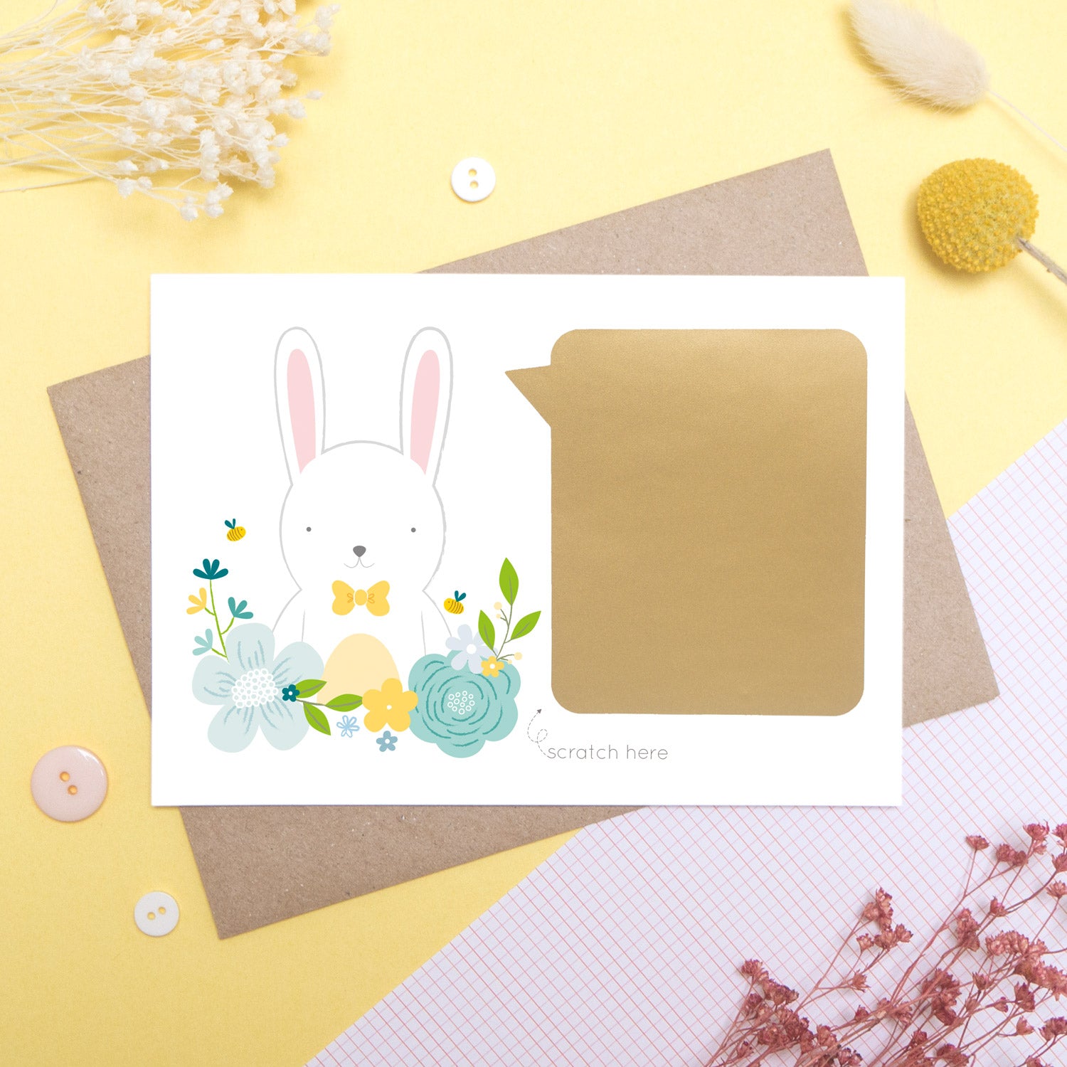 A personalised godparent scratch card before it has been scratched off. This is how the cards will arrive. This one has been shot on a yellow background with floral props. It features a white rabbit with a blue theme.