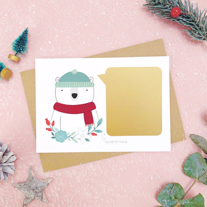 A personalised polar bear scratch card shot on a pink background with festive props in grey and green. Here the gold panel has been fixed and is ready to be scratched.