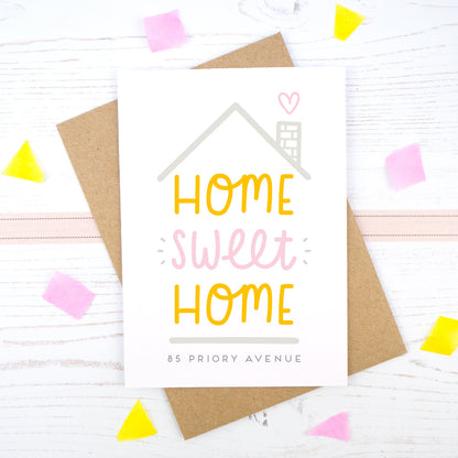 Home Sweet Home is a personalised card featuring the property number and road name. This version has a grey roof, a heart coming from the chimney and has 'home sweet home' in pink and orange.
