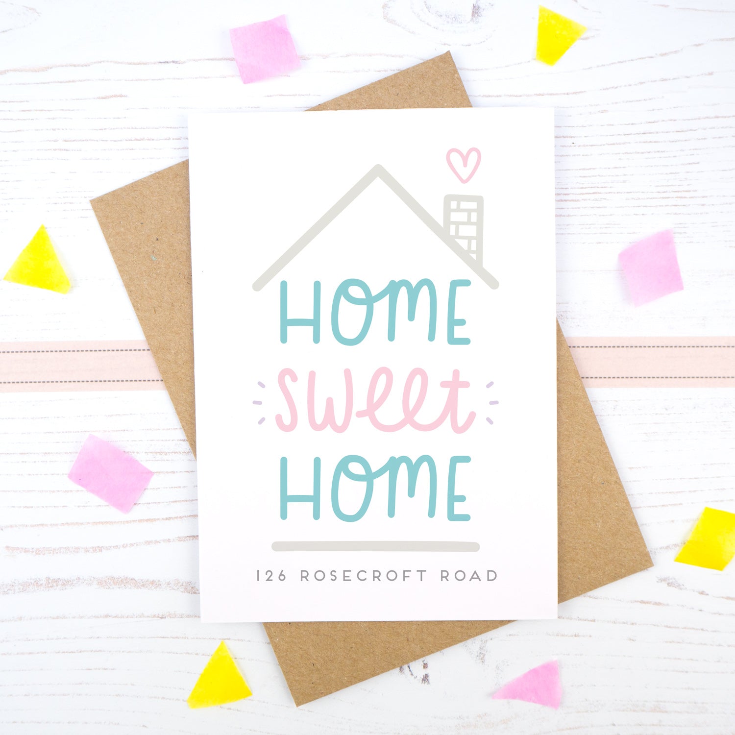 Home Sweet Home is a personalised card featuring the property number and road name. This version has a grey roof, a heart coming from the chimney and has 'home sweet home' in teal and pink.