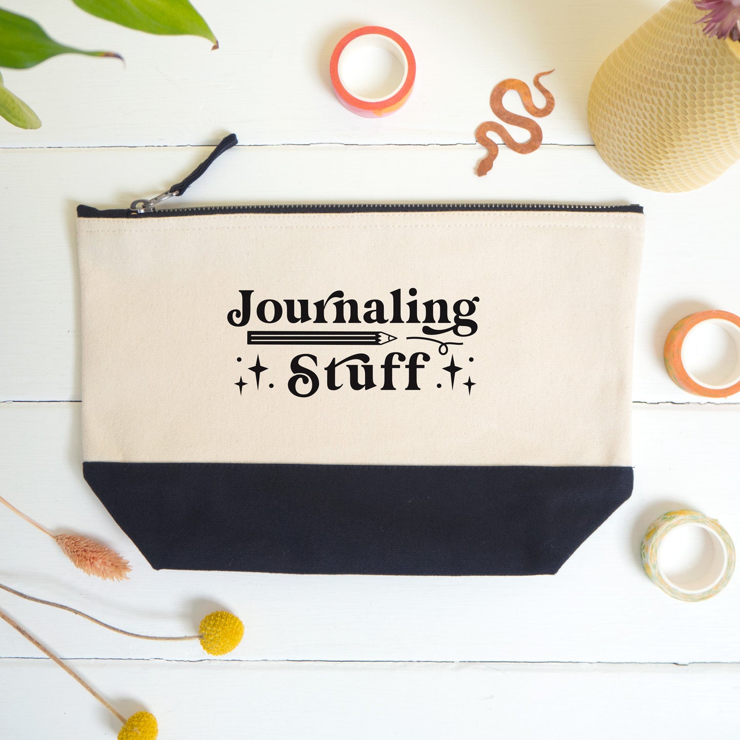 A flatlay view of the journaling stuff project bag shot on a white surface surrounded by dry flowers, washi and a snake bookmark.