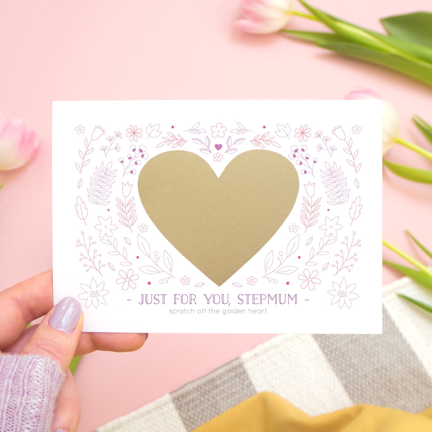 A personalised just for you stepmum scratch card showing how the card looks before the golden heart is scratched off to reveal the message. Shot on a pink background with tulips.