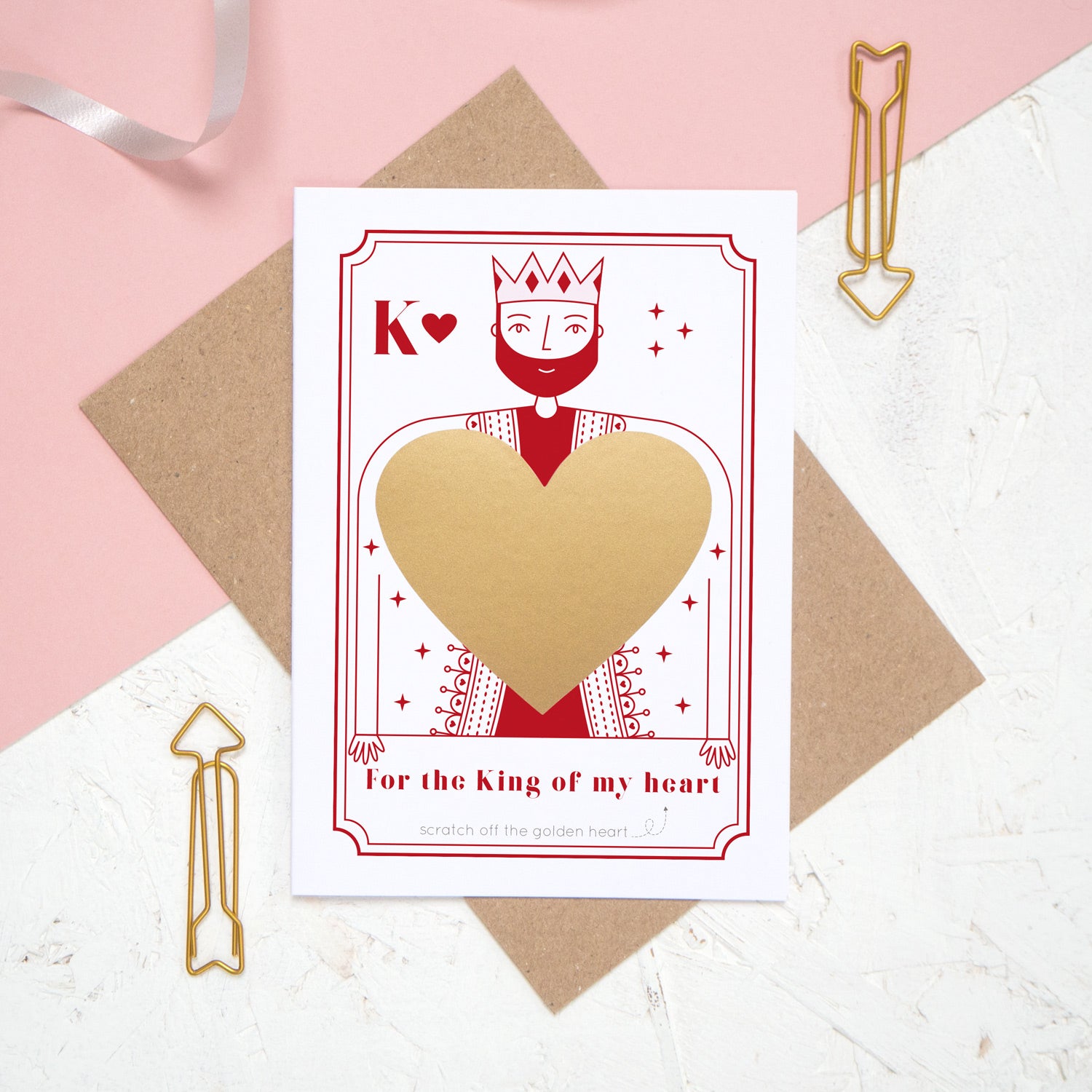 A king of my heart scratch and reveal card featuring a gold panel hiding the secret message. Shot on a pink background.