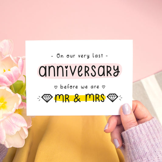 A last anniversary or Valentine’s card photographed on a pink background with pink tulip flowers, a grey and white stripe rug and yellow fabric. This image shows the last anniversary option with the Mr & Mrs wording. The text is black and there are pops of yellow and pink behind key words.