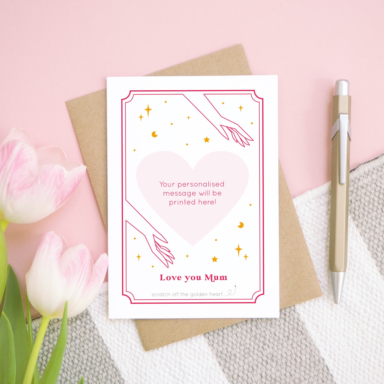 A personalised 'love you...' scratch card showing what the card will look like if all of the heart is scratched off. It has been shot on a pink background, with tulips and a pen for scale.