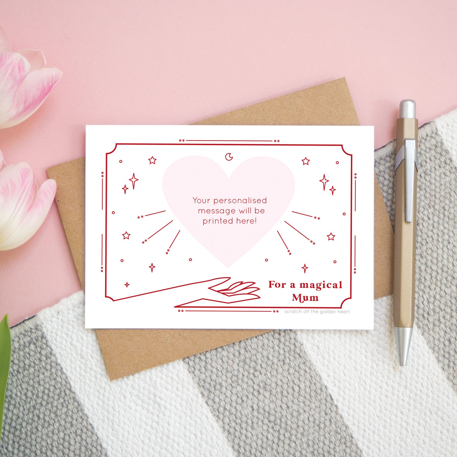 A personalised 'magical mum' scratch card showing how the card will look once all of the gold heart has been removed. The card is shot from above on a pink, white and grey background with a pen for scale.