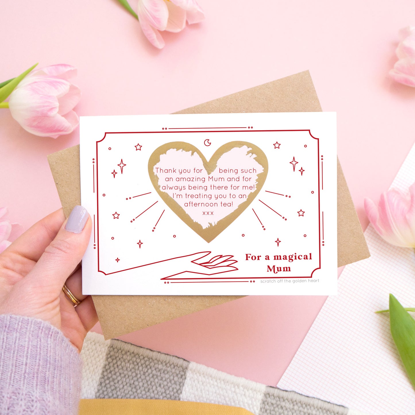 A personalised 'magical mum' scratch card showing how your personalised message could look with the gold heart scratched off. The card is being held over a pink background with pink tulips.