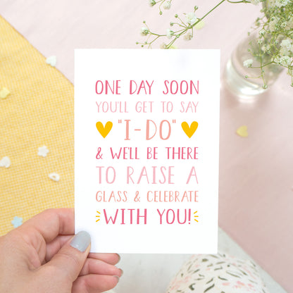 One day soon postponed wedding card in tones of pink. Photographed on a white, yellow and pink background with flowers poking in the top right hand side.