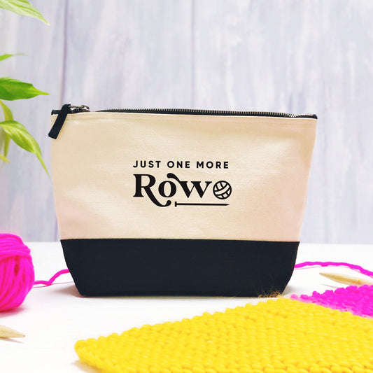 A 'just one more row' cotton storage bag, natural in colour with a black box bottom base photographed on a purple background with leaves, and a ball of pink wool with a knitting project.