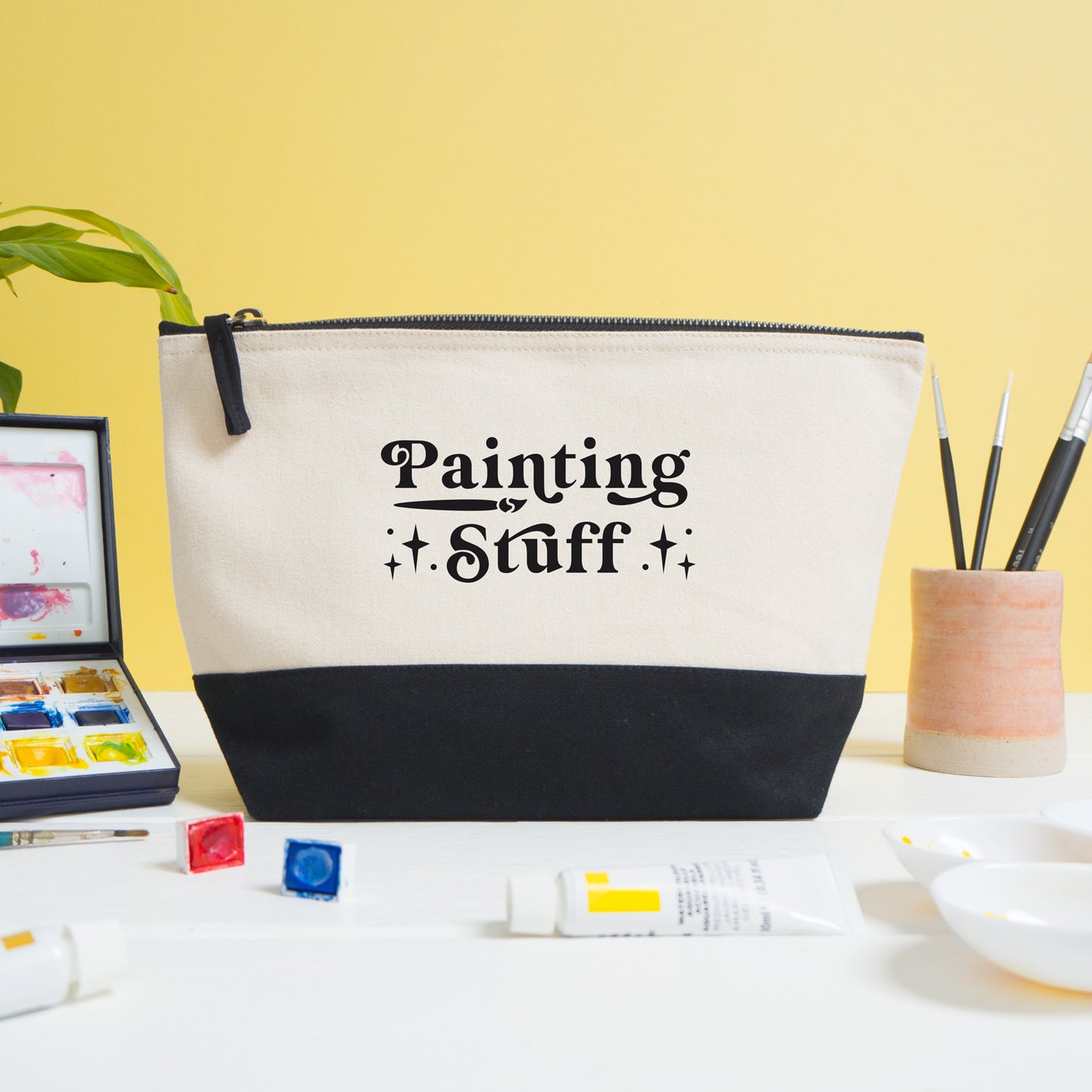 A painting stuff project bag shot on a white and yellow background with painting materials in the foreground.