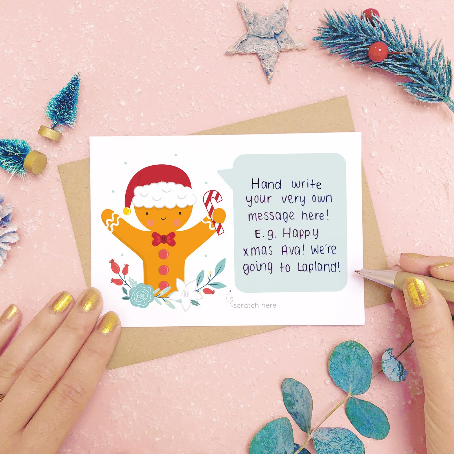 A personalised Gingerbread man scratch card showing where to write the hand written message. Shot on a pink background with grey and green festive props.