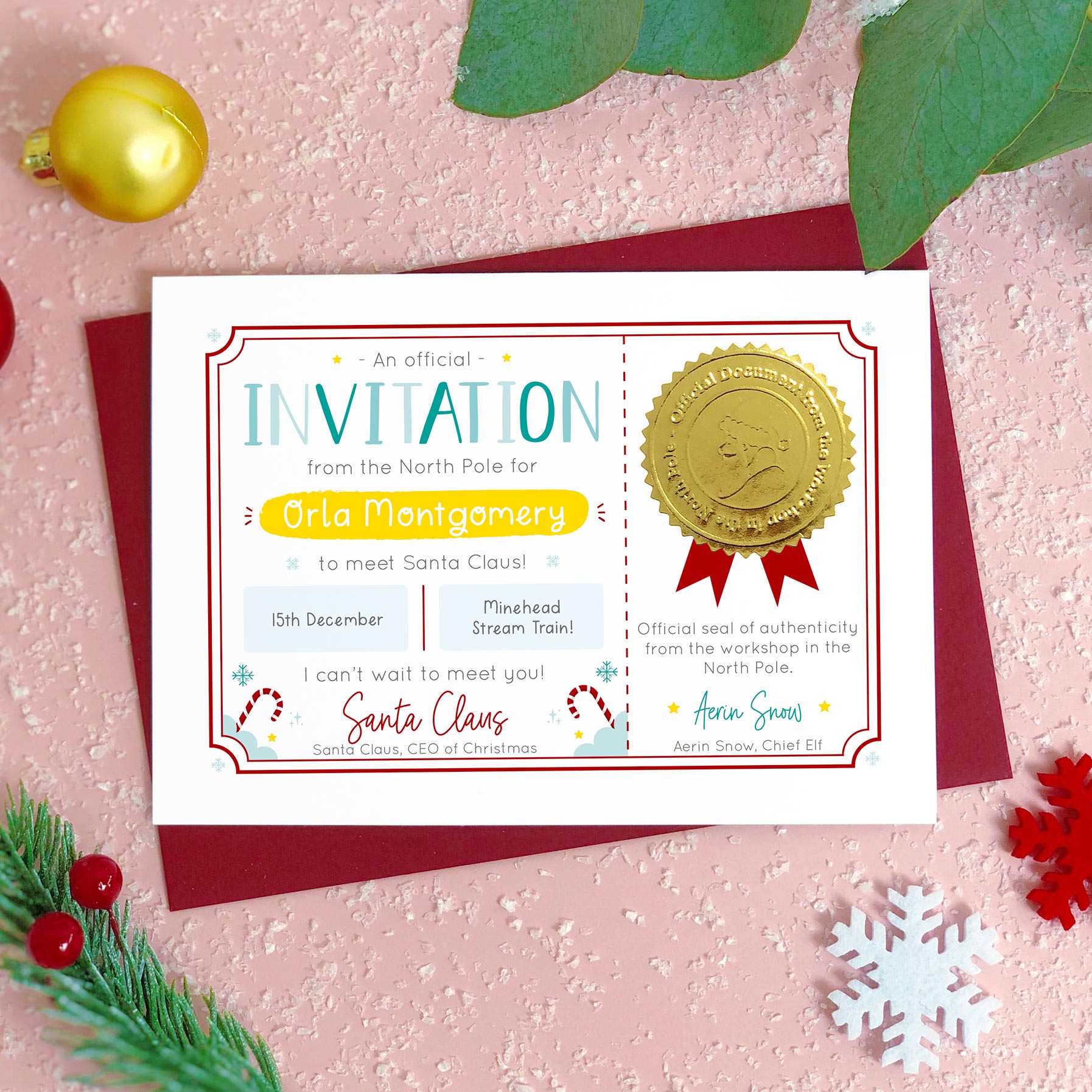 A personalised invitation certificate to visit Santa (or Father Christmas) photographed flat lay style on top of a pink background covered in ‘snow’, pieces of foliage, snowflakes and a bauble. The card is personalised with a childs name, date of the visit to meet Father Christmas and the location. It also features a shiny gold seal with the face of a santa character.