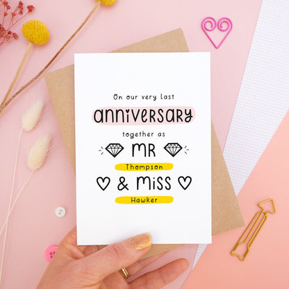 A personalised last anniversary or Valentine’s card photographed on a pink background with floral props, paper clips, and buttons. This image shows the last anniversary option with the Mr & Miss wording. The text is black and there are pops of yellow and pink behind key words.