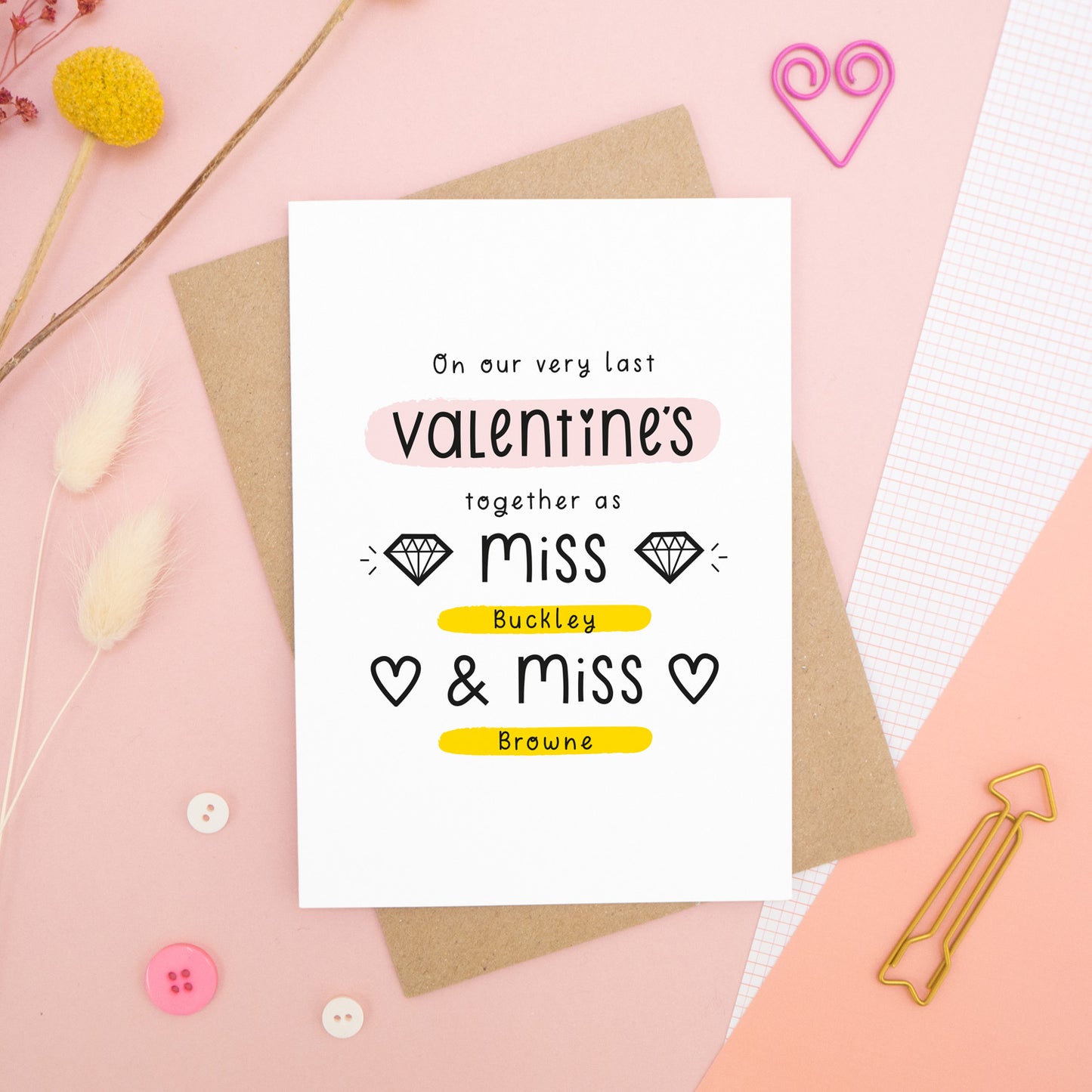 A personalised last anniversary or Valentine’s card photographed on a pink background with floral props, paper clips, and buttons. This image shows the last valentine’s option with the Miss & Miss wording. The text is black and there are pops of yellow and pink behind key words.