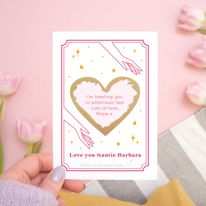 A personalised 'love you...' scratch card with the gold heart scratched off revealing the personalised message. The card is photographed held over a pink background with tulips!