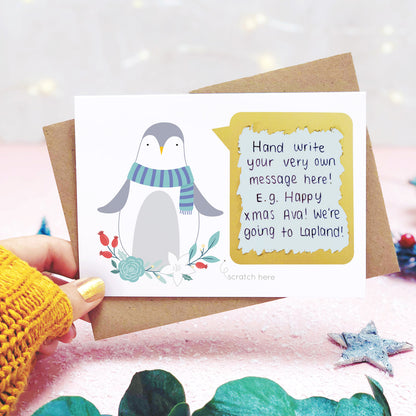 Personalised penguin scratch card shot on a light pink background behind eucalyptus with the scratch off message revealed.