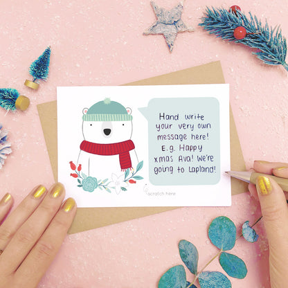 A personalised polar bear scratch card shot on a pink background with festive props in grey and green. This is an example of where to write your hidden message.