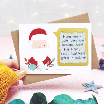 A personalised santa scratch card being held behind eucalyptus leaves, on a pink background with the scratch off message revealed 