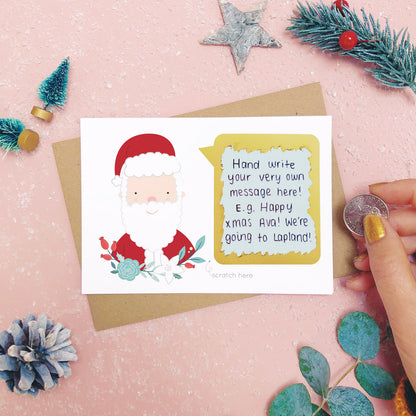 An example of a handwritten message on a personalised scratch card after it has been scratched off with a coin.. Shot on a pink background with festive photo props.