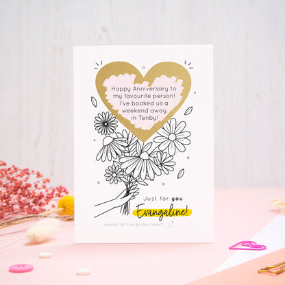 A personalised flower bouquet scratch card photographed on a pink and white background with floral props, paper clips, and buttons. This card shows a black and white floral illustration and the golden heart after it has been scratched off to reveal the secret message!