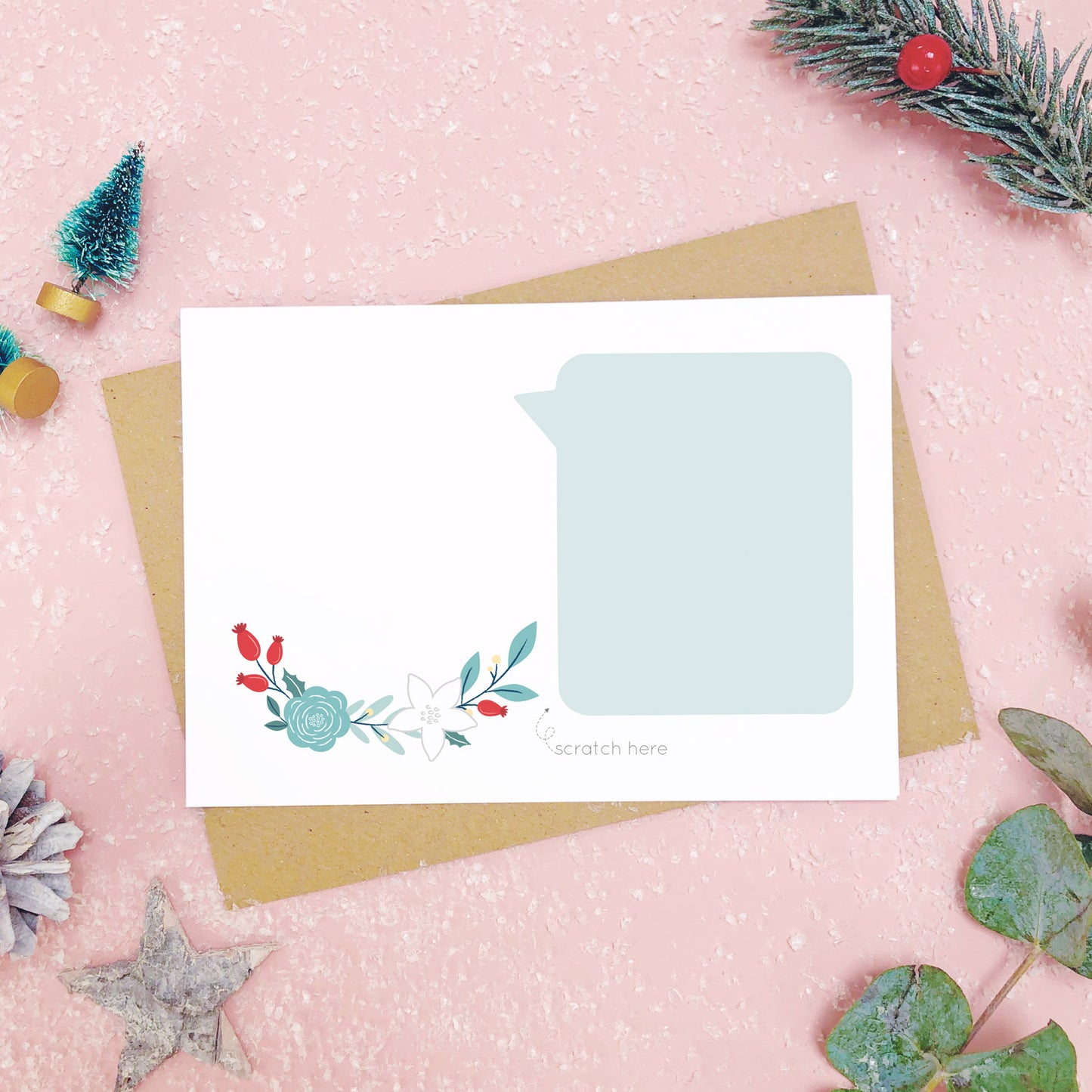 A make your own scratch card with a blank area for drawing and blank speech bubble for writing your message. Shot on pink with snow and greenery.