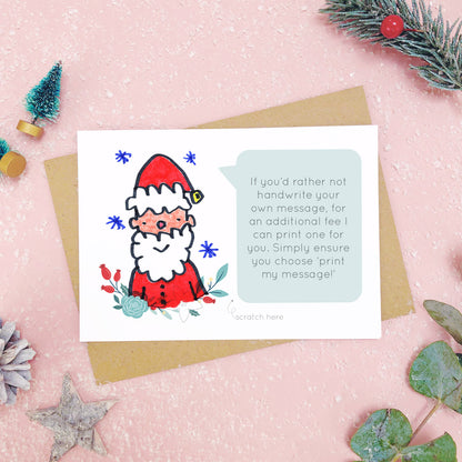 A make your own scratch card with a childs drawing of santa and an example of a printed message. Shot on pink with snow and greenery.