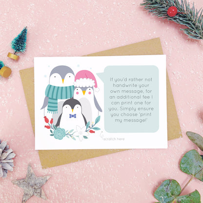 A personalised penguin family scratch card an example of the printed message. Shot on a pink background with grey and green festive props.
