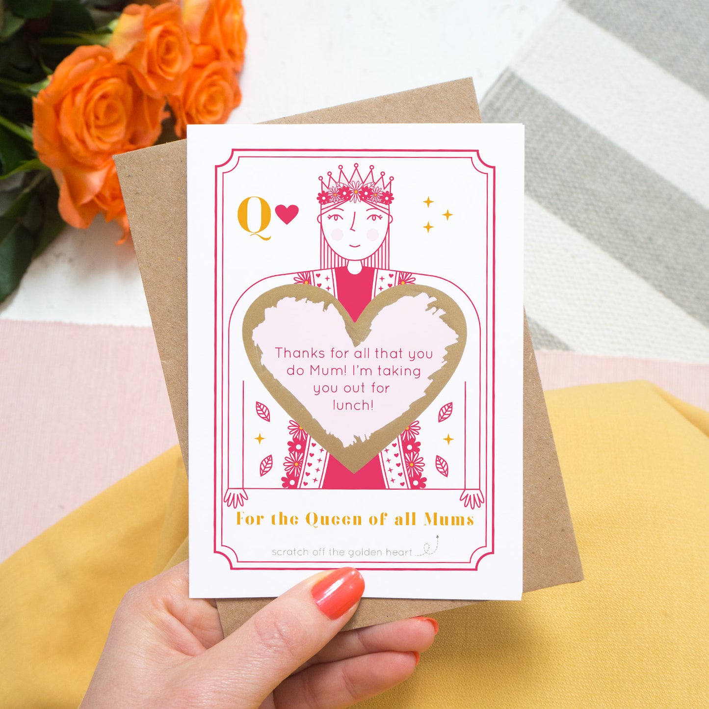 A queen of all mums scratch card showing you where your printed personalisation will go on the card. The card has been scratched off revealing the personalisations and is being held above pink tulips and a yellow skirt.