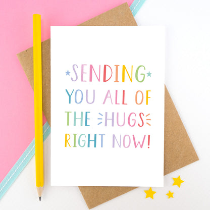Sending you all of the hugs right card photographed on a pink and white background with a teal ribbon and a bright yellow pencil. This image shows the letters in a rainbow palette.