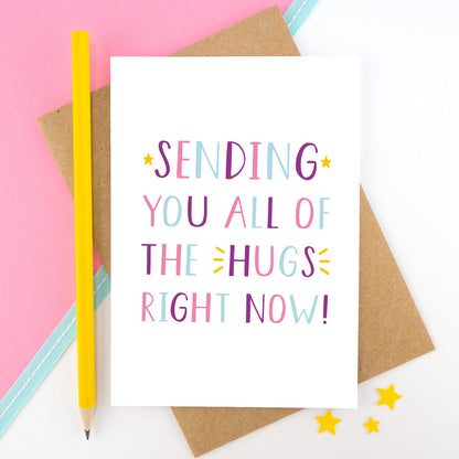 Sending you all of the hugs right card photographed on a pink and white background with a teal ribbon and a bright yellow pencil. This image shows the letters in a pink, purple and blue palette.